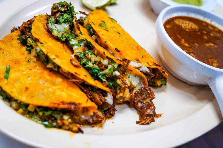 Quesabirria tacos with melted cheese, onion, cilantro, and a cup of consomme