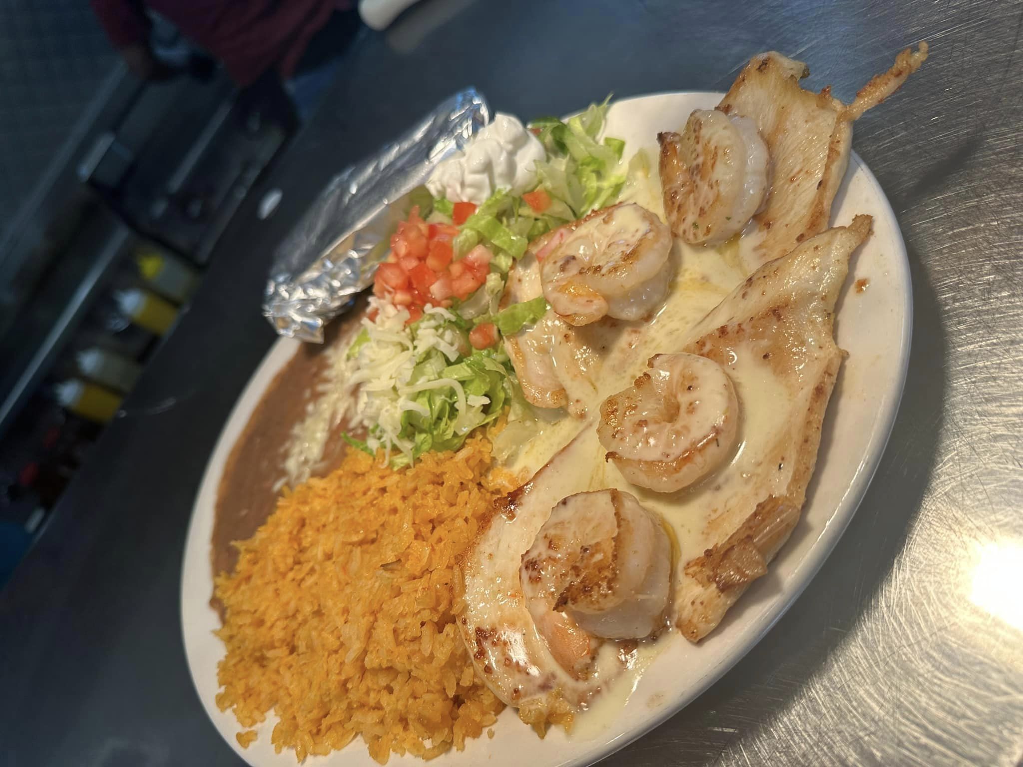 Shrimp tacos on a plate with rice, beans, lettuce, and sour cream